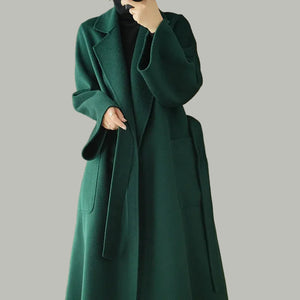 Person wearing a long green coat in a room with wooden walls and a beige chair.