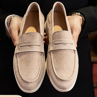 Pair of beige loafers held by a person wearing black pants.