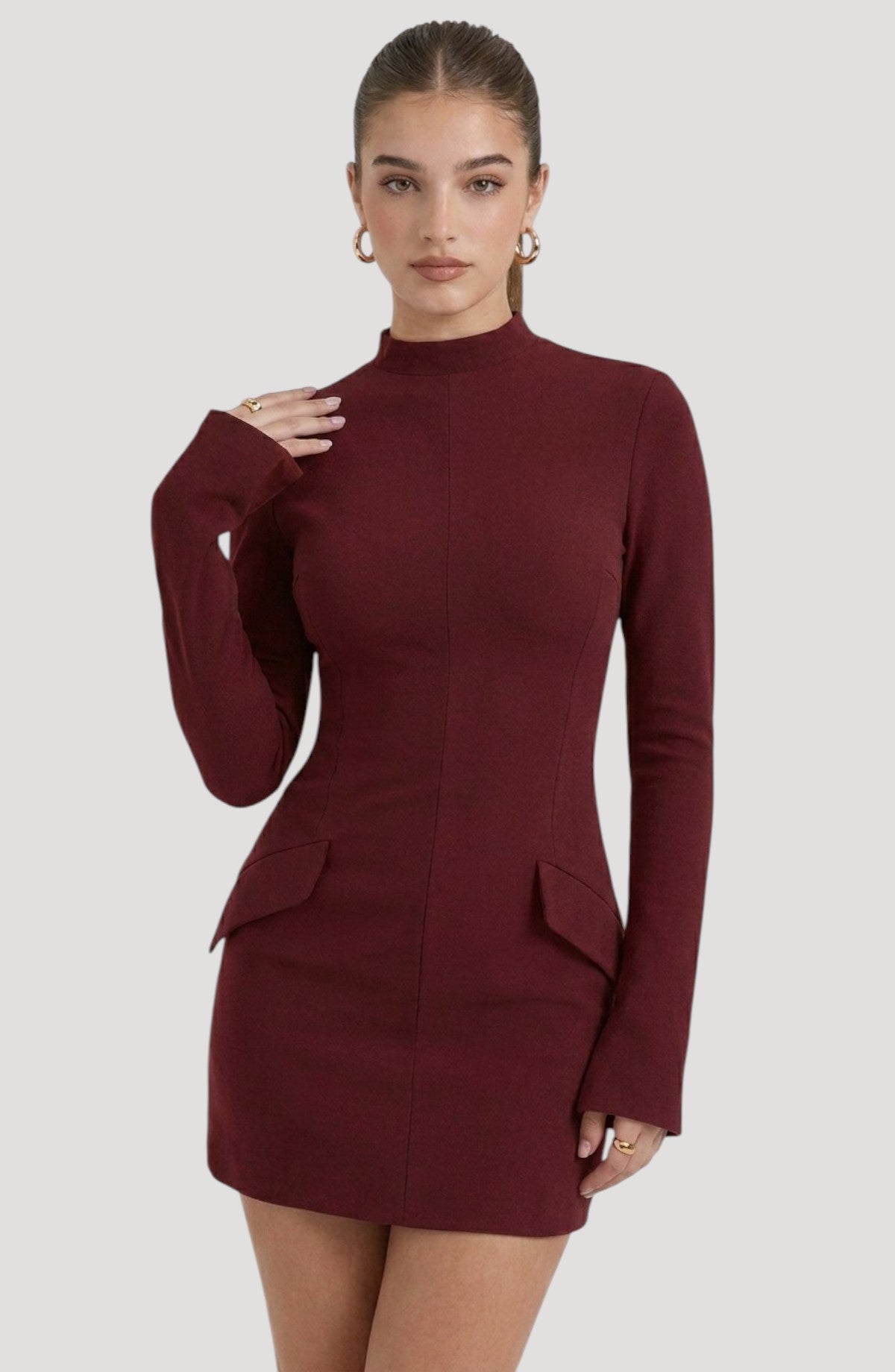 LORVENES burgundy long-sleeve mini dress with mock neck and flap pockets. Model wears gold hoop earrings and rings.