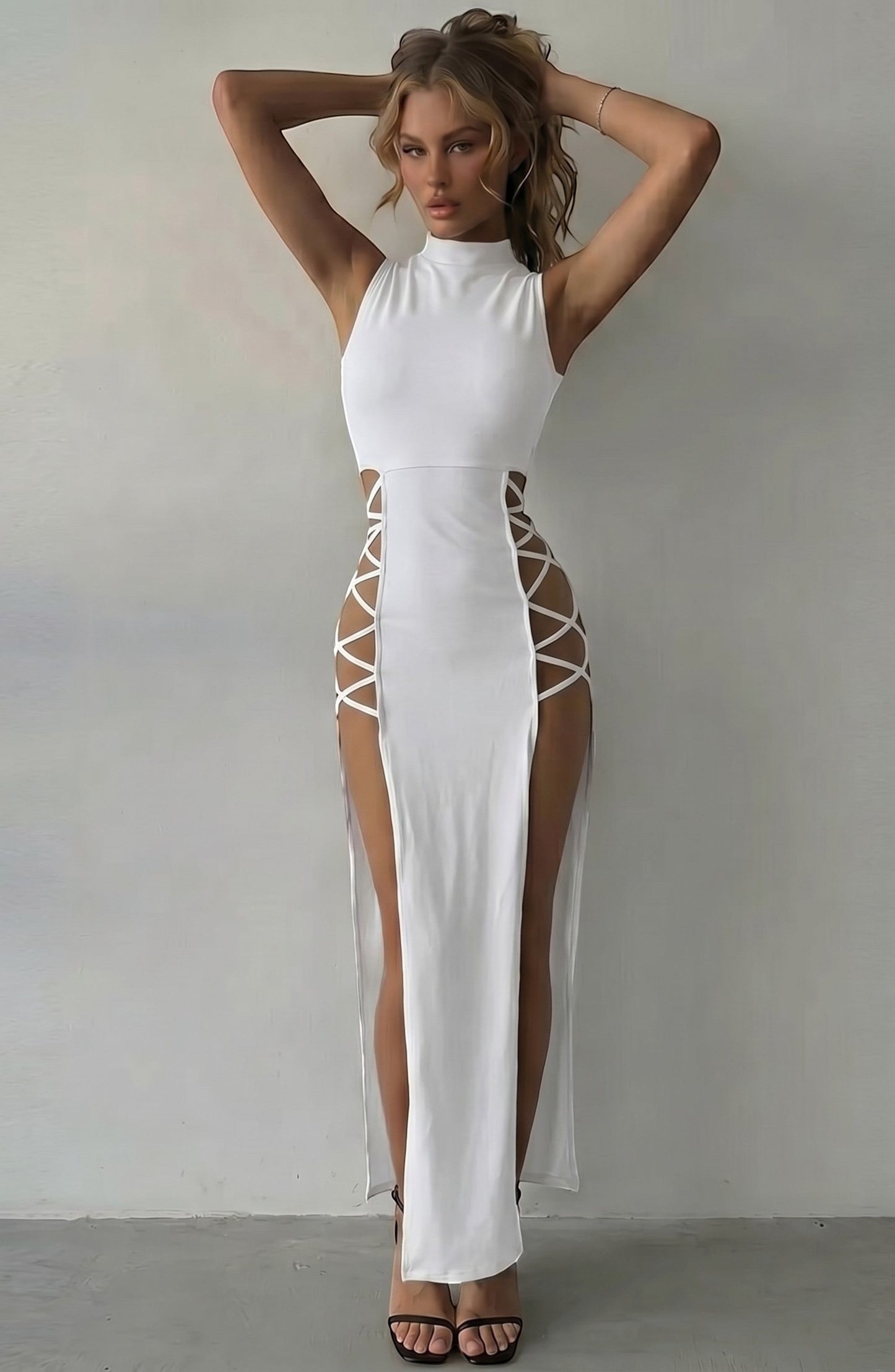 LORVENE white sleeveless mock neck maxi dress with daring lace-up side cutouts and high slits. Model wears heels.